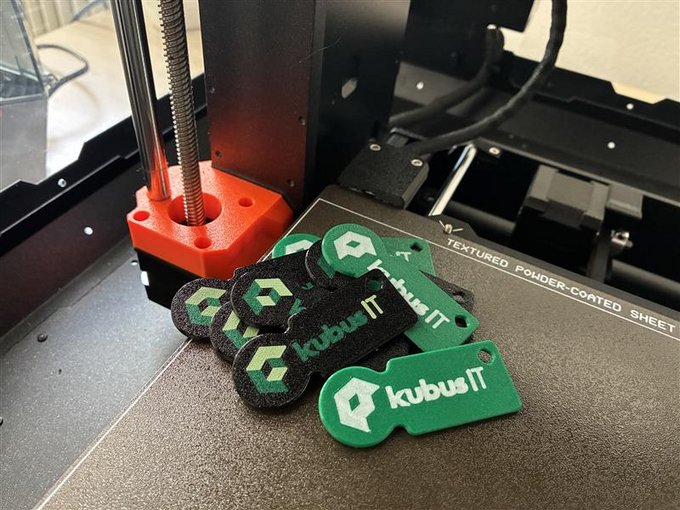 3D-gedruckte Einkaufswagenchips mit kubus IT Logo Mehrere grüne und schwarze Einkaufswagenchips mit kubus IT Logo liegen auf der Druckplatte eines 3D-Druckers.