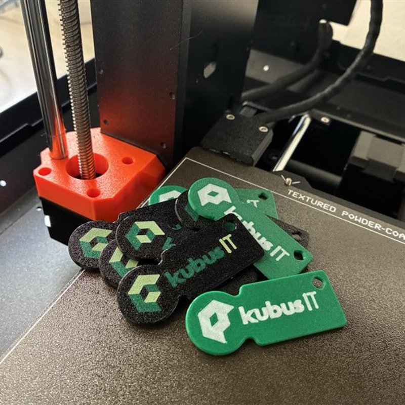 3D-gedruckte Einkaufswagenchips mit kubus IT Logo Mehrere grüne und schwarze Einkaufswagenchips mit kubus IT Logo liegen auf der Druckplatte eines 3D-Druckers.