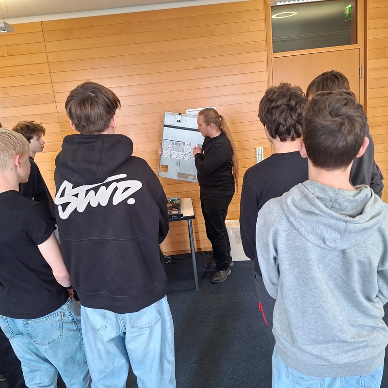 Schüler erhalten Einblick in Computertechnik bei kubus IT Eine Gruppe von Schülerinnen und Schülern steht in einem Raum und hört einer Person zu, die ein geöffnetes Computergehäuse erklärt und technische Komponenten zeigt