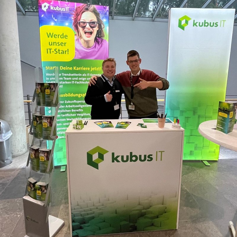 2 Mitarbeiter stehen am Messestand und lächeln in die Kamera 2 Mitarbeiter stehen am Messestand der kubus IT und lächeln in die Kamera